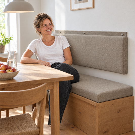 Vrouw aan de eettafel met muurkussen op maat in camel als rugleuning boven de eikenhouten bank