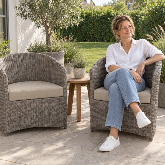 Lachende vrouw in een rotan fauteuil op een halfrond lounge zitkussen op maat voor buiten in beige op het terras